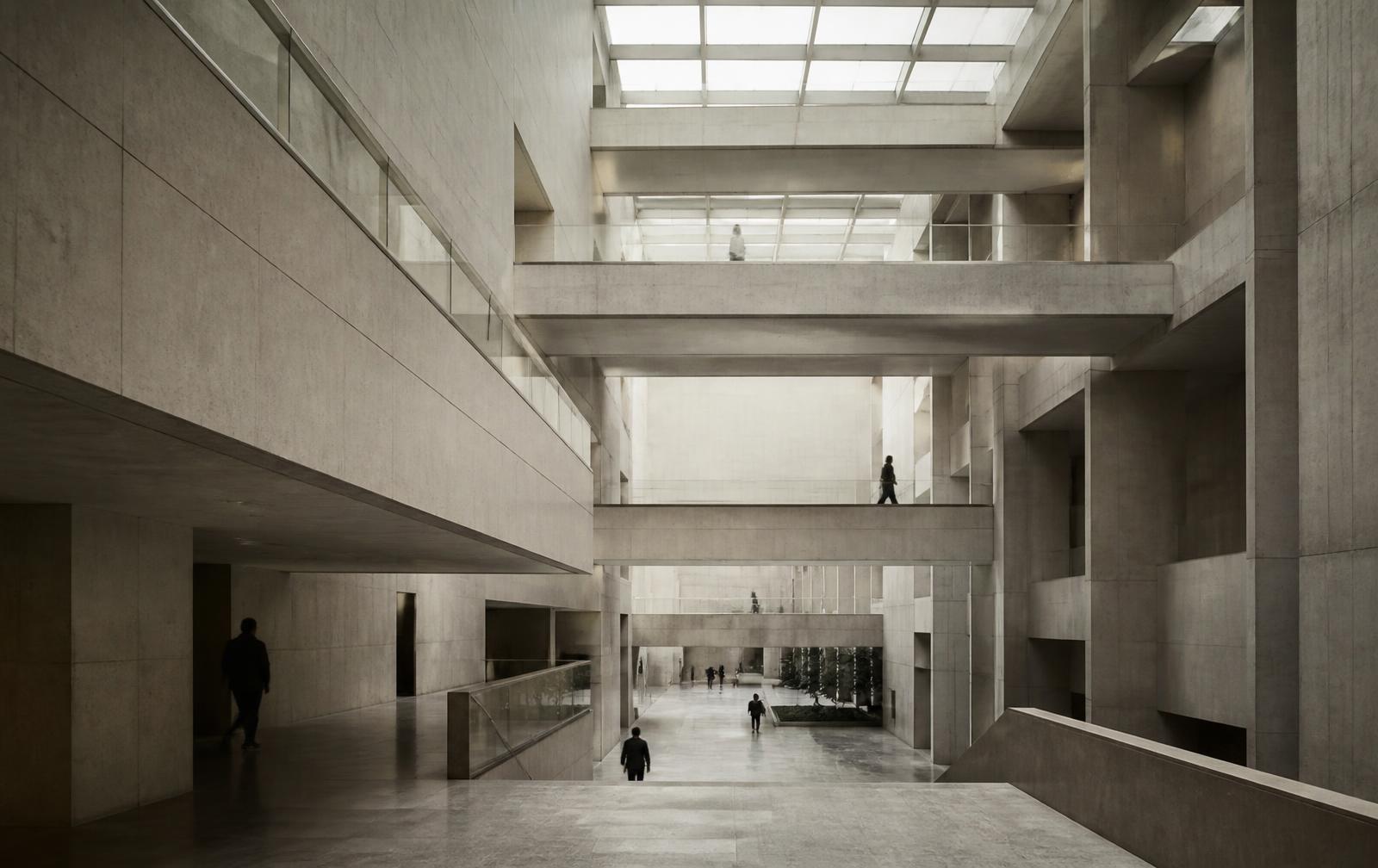 People moving across the layered walkways of a large institutional building in flat daylight