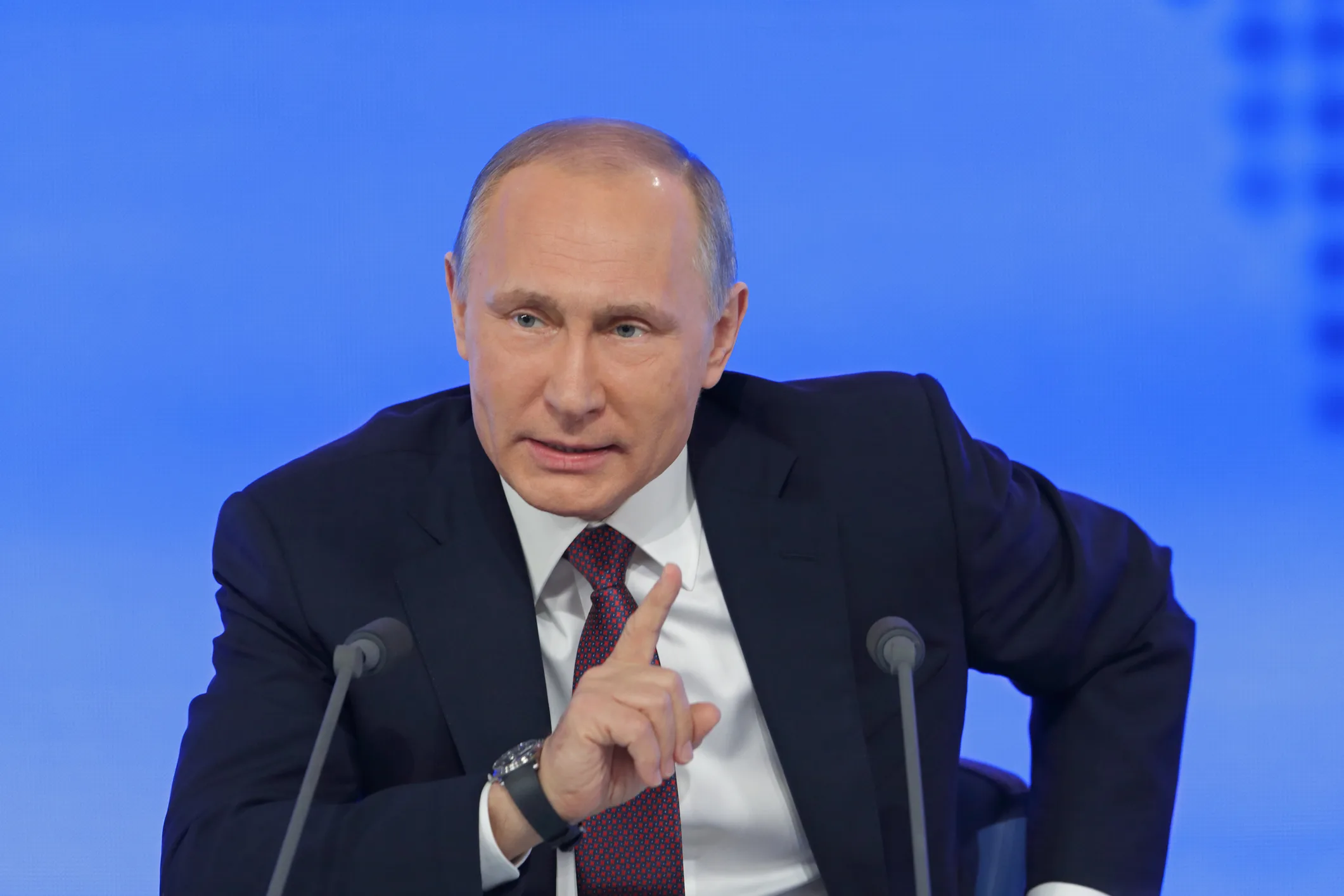 Russian President Vladimir Putin gesturing with his finger while speaking at a press conference or public event.