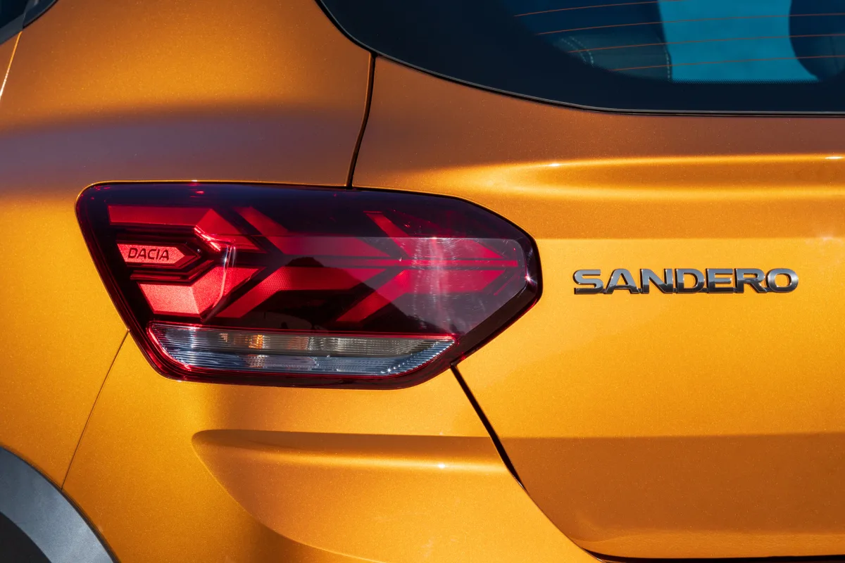 Close-up of the rear of a yellow Dacia Sandero, showing the distinctive Y-shaped LED taillight and the 'SANDERO' and 'DACIA' badges.