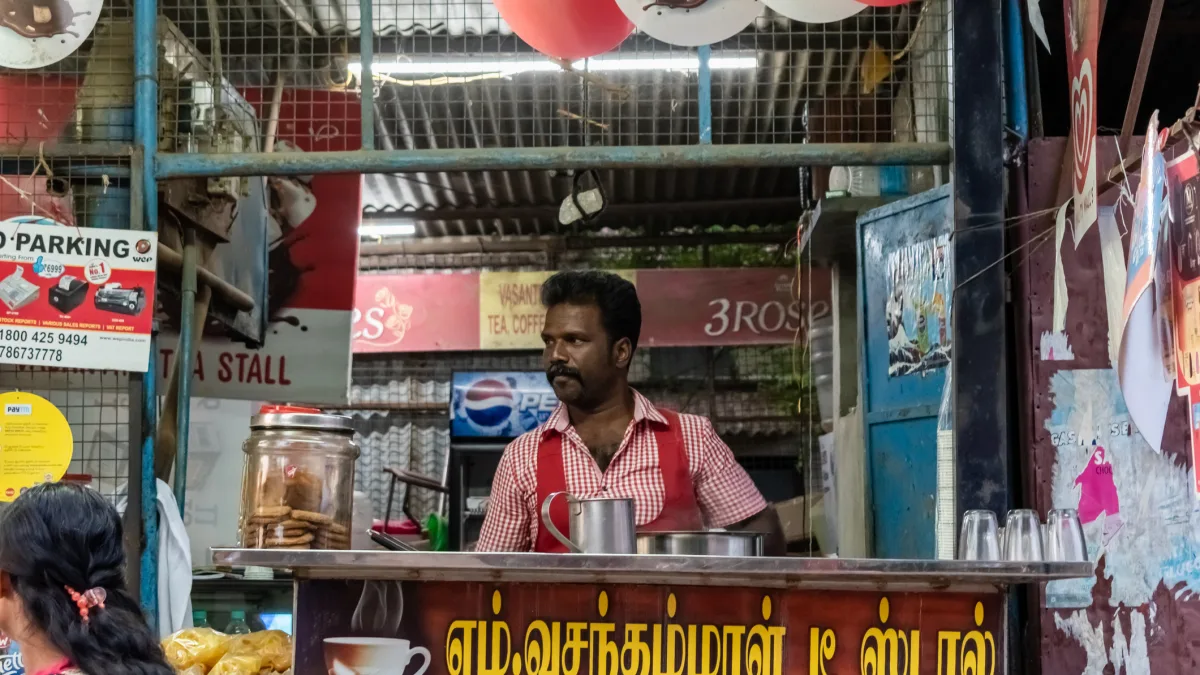 Man running a traditional Indian tea stall with biscuits and metal cups in a local market