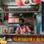 Man running a traditional Indian tea stall with biscuits and metal cups in a local market