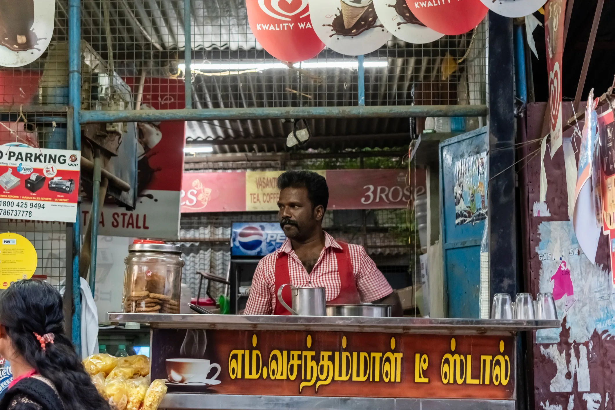 Man running a traditional Indian tea stall with biscuits and metal cups in a local market