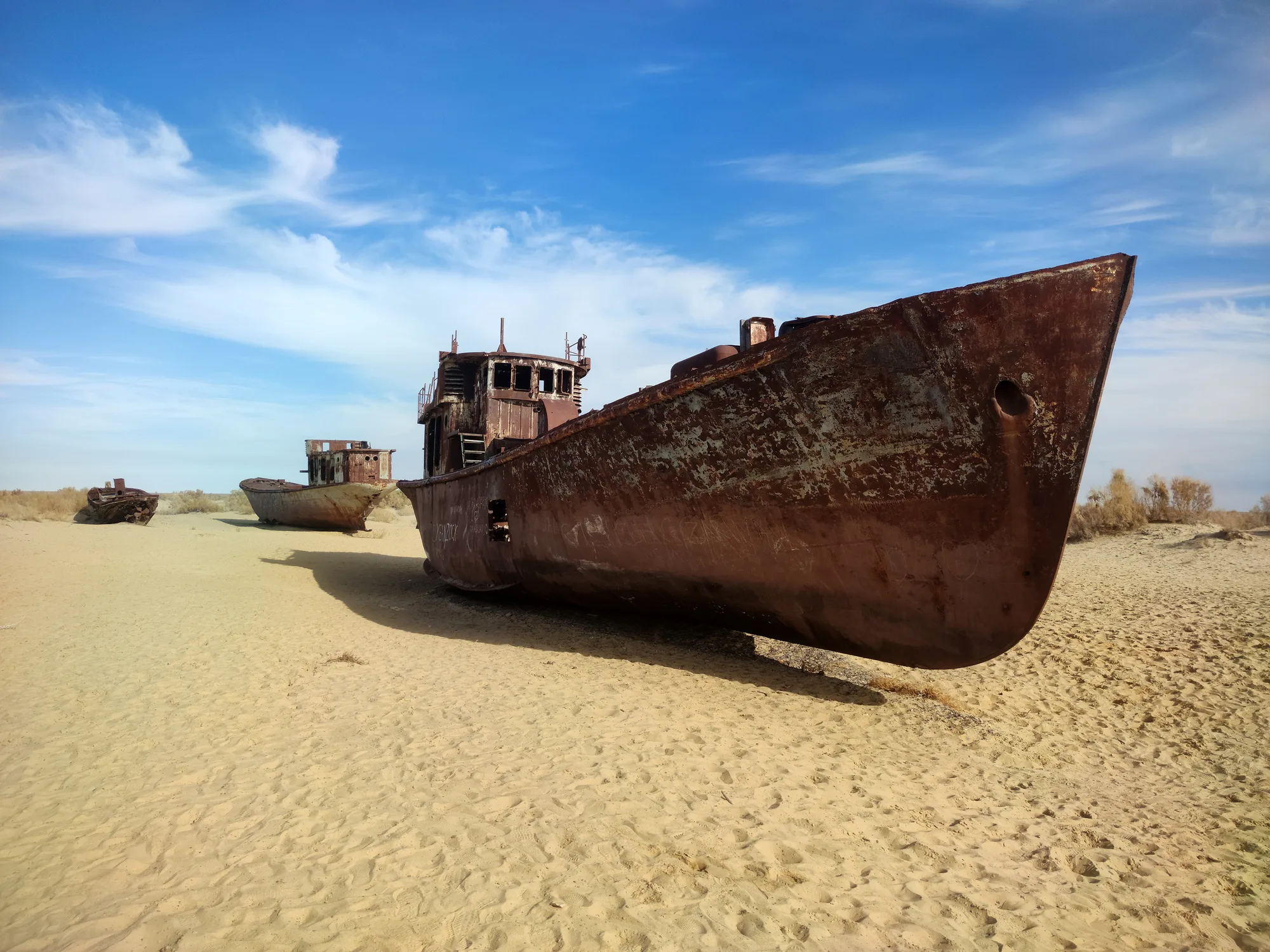 A rusted shipwreck stranded on a dry, sandy desert landscape under a blue sky, symbolizing climate change and the Aral Sea disaster.