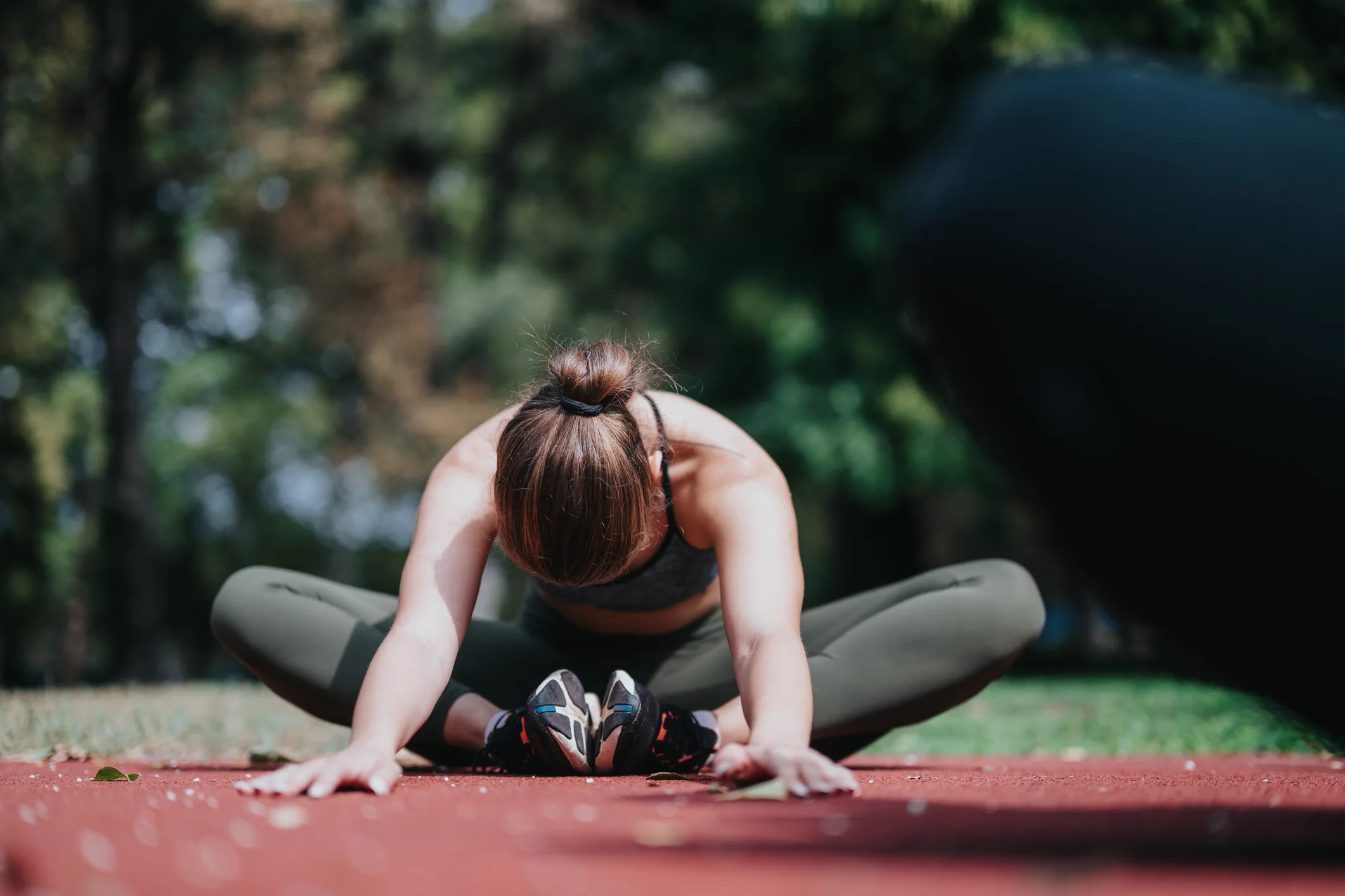 A woman stretches on a running track, performing a seated butterfly stretch for flexibility.