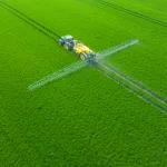 A modern tractor spraying crops in a lush green field in Poland, showcasing precision agriculture and climate-smart farming practices.