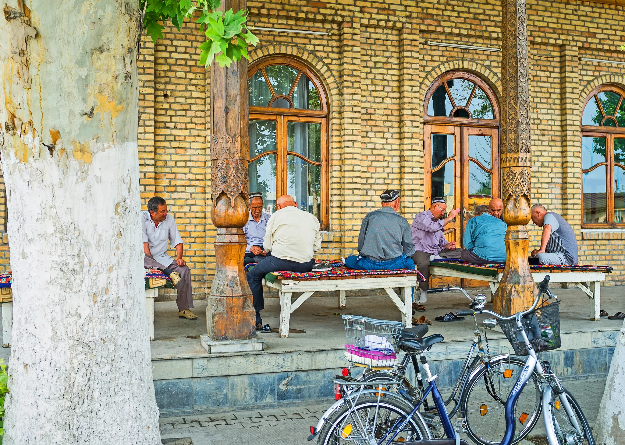 Elderly men in traditional caps gathered on benches outside a historic brick building in Central Asia, symbolizing community dialogue, cultural heritage, and growing regional cooperation