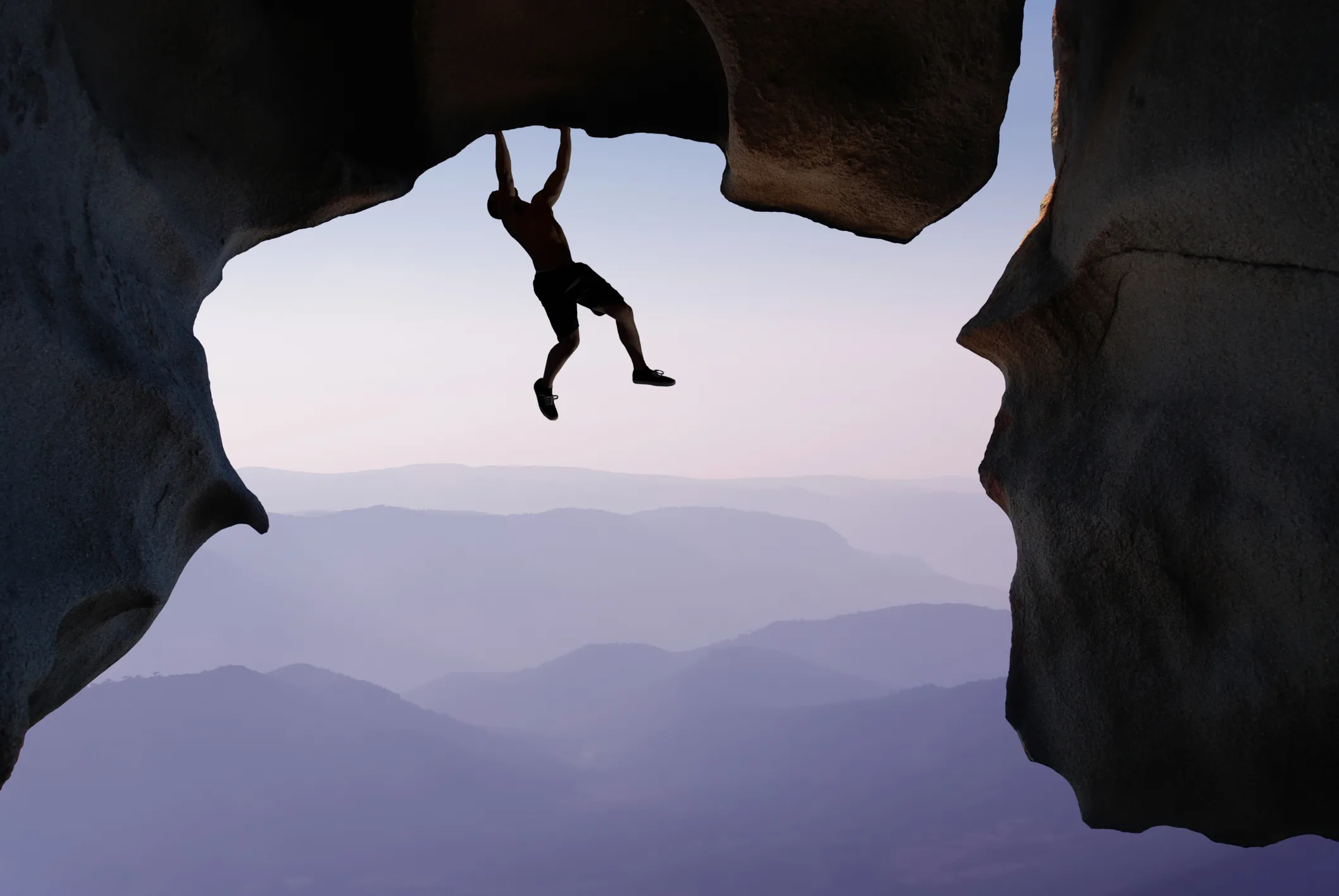 Man hanging from a cliff edge, symbolizing courage, risk-taking, and the journey of personal reinvention.