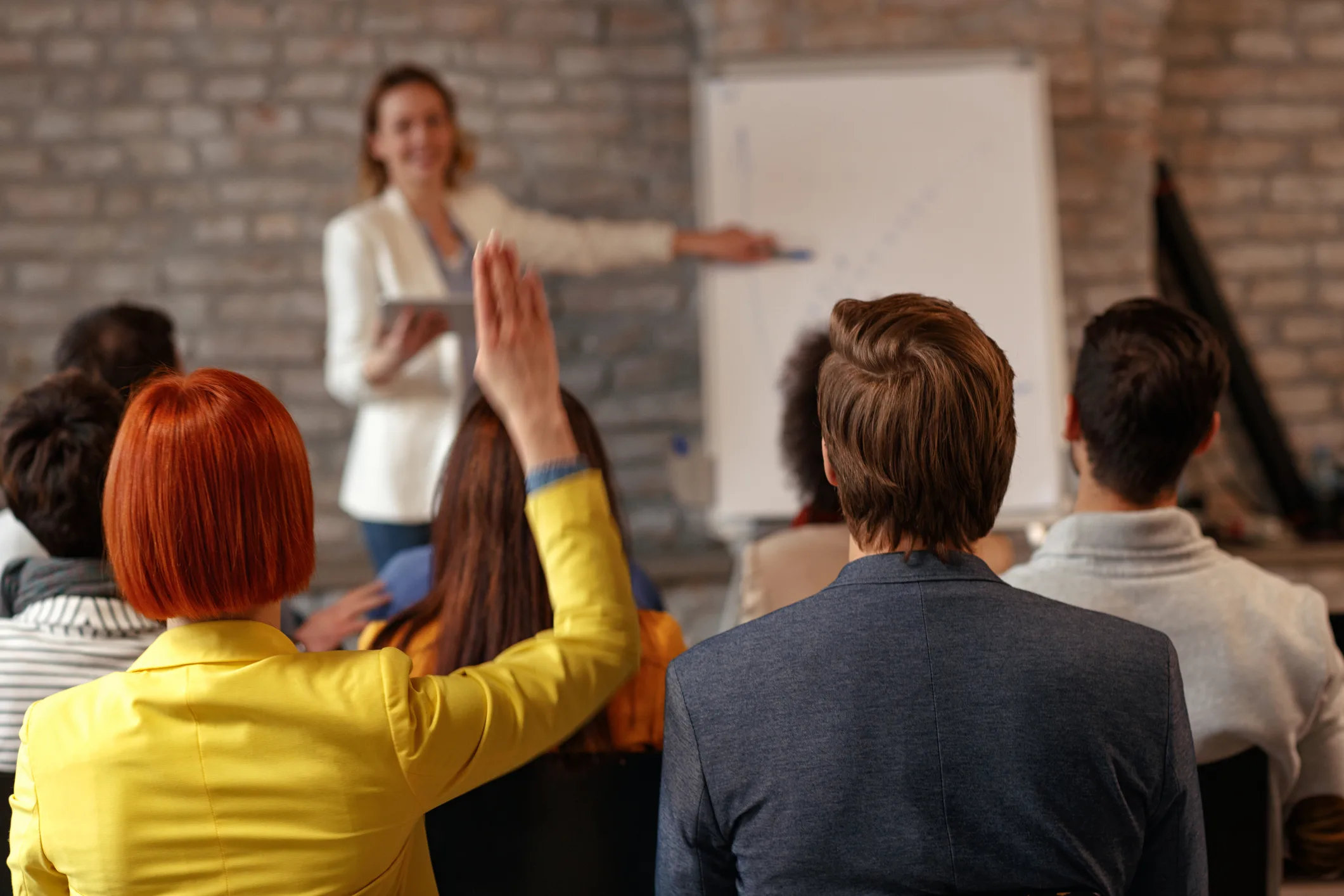 Business workshop with participants asking questions while a speaker presents strategy on a whiteboard, highlighting the importance of asking the right questions in reinvention.