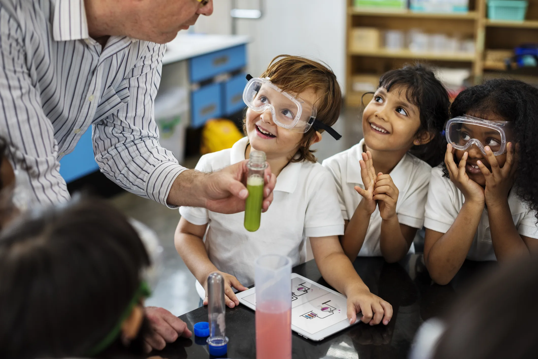 Teacher showing science experiment to smiling students wearing safety goggles, representing future skills and STEM education in “Tomorrow’s Workers Today.”